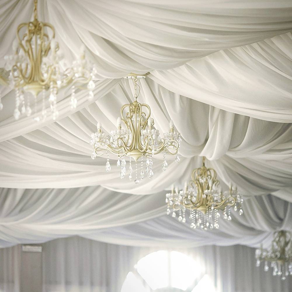 Elegant wit gedrapeerd plafond met sierlijke kroonluchters die een verfijnde sfeer creëren.