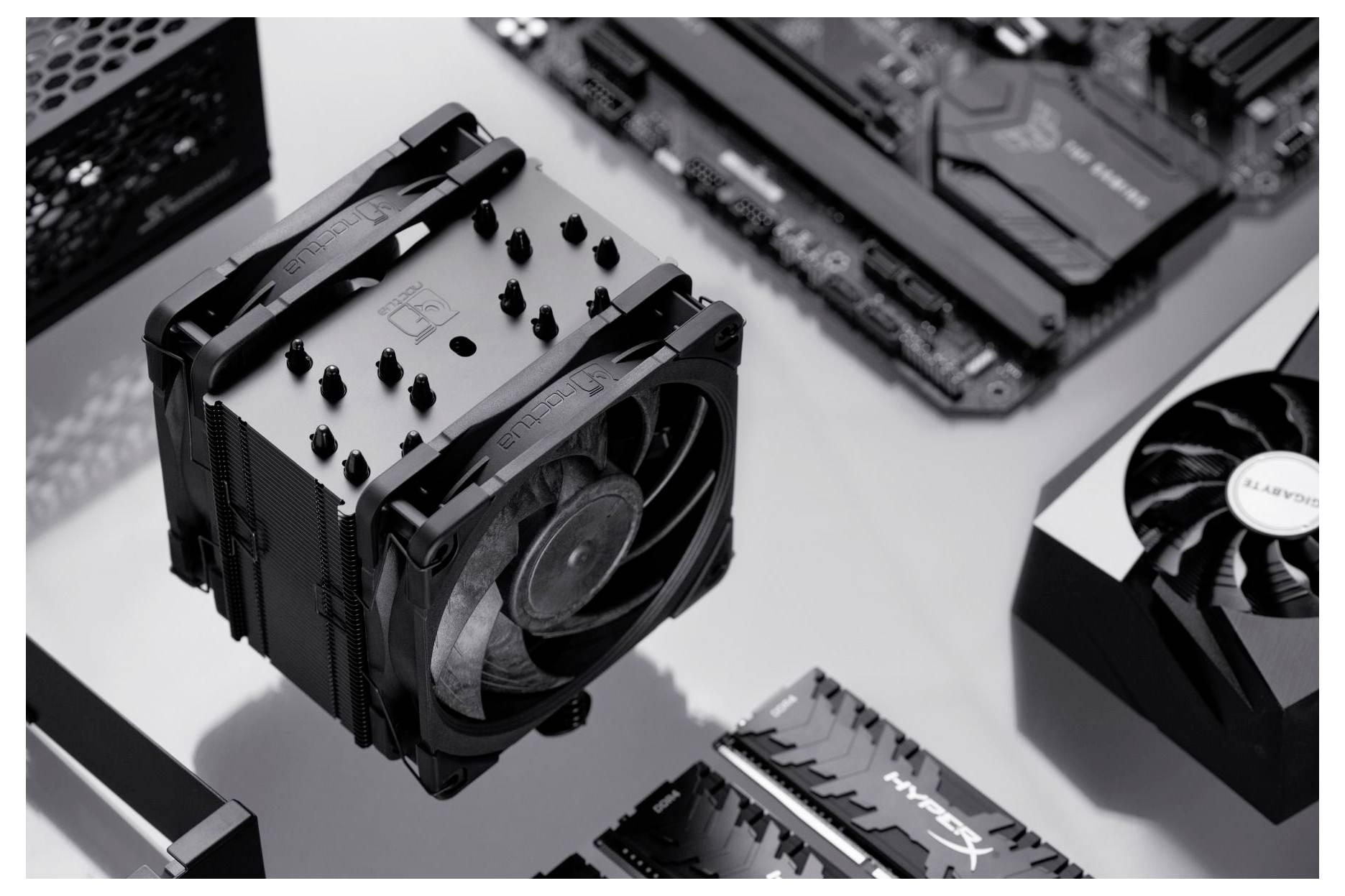 Een zwart-wit foto die computercomponenten toont, waaronder een CPU-koeler, videokaart, moederbord en RAM-modules.