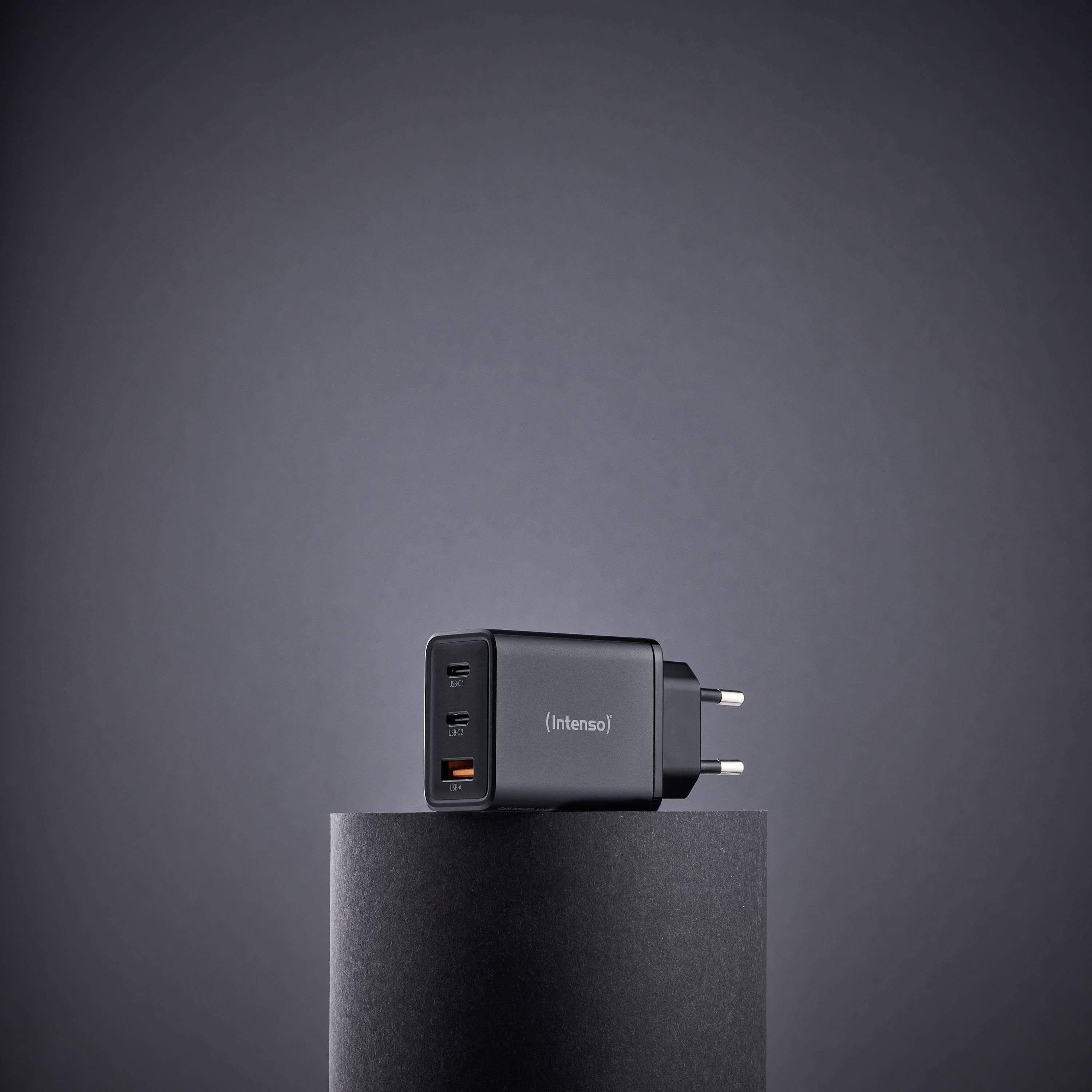 Een zwarte USB-wandlader met meerdere poorten staat op een cilindrische sokkel tegen een effen grijze achtergrond.