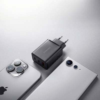 Twee smartphones, één zilver met drie camera's en één wit met twee camera's, liggen naast een zwarte USB-oplader met meerdere poorten.