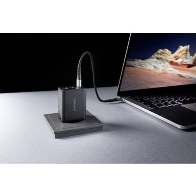 Een draagbare powerbank laadt een laptop op aan een grijze tafel. Het laptopscherm toont een landschapsafbeelding.