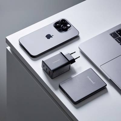 Een smartphone, een laptop, een draagbare oplader en een USB-adapter zijn netjes op een tafel gerangschikt, wat een minimalistische technische setup laat zien.