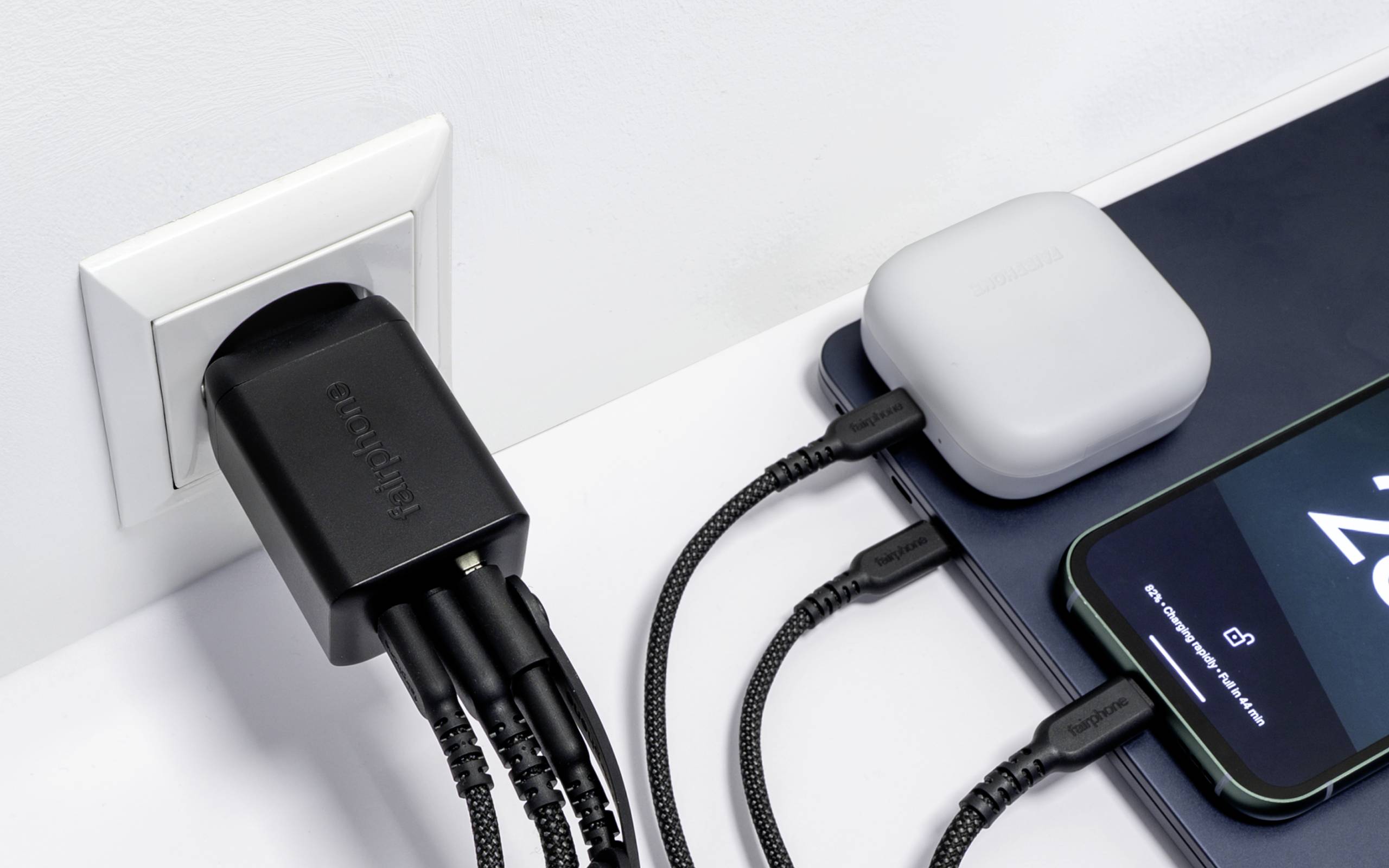 Een wandcontactdoos met een multi-poort oplader voedt een smartphone, laptop en een draadloze oordoppen-etui, waarbij verschillende apparaten gelijktijdig worden opgeladen.