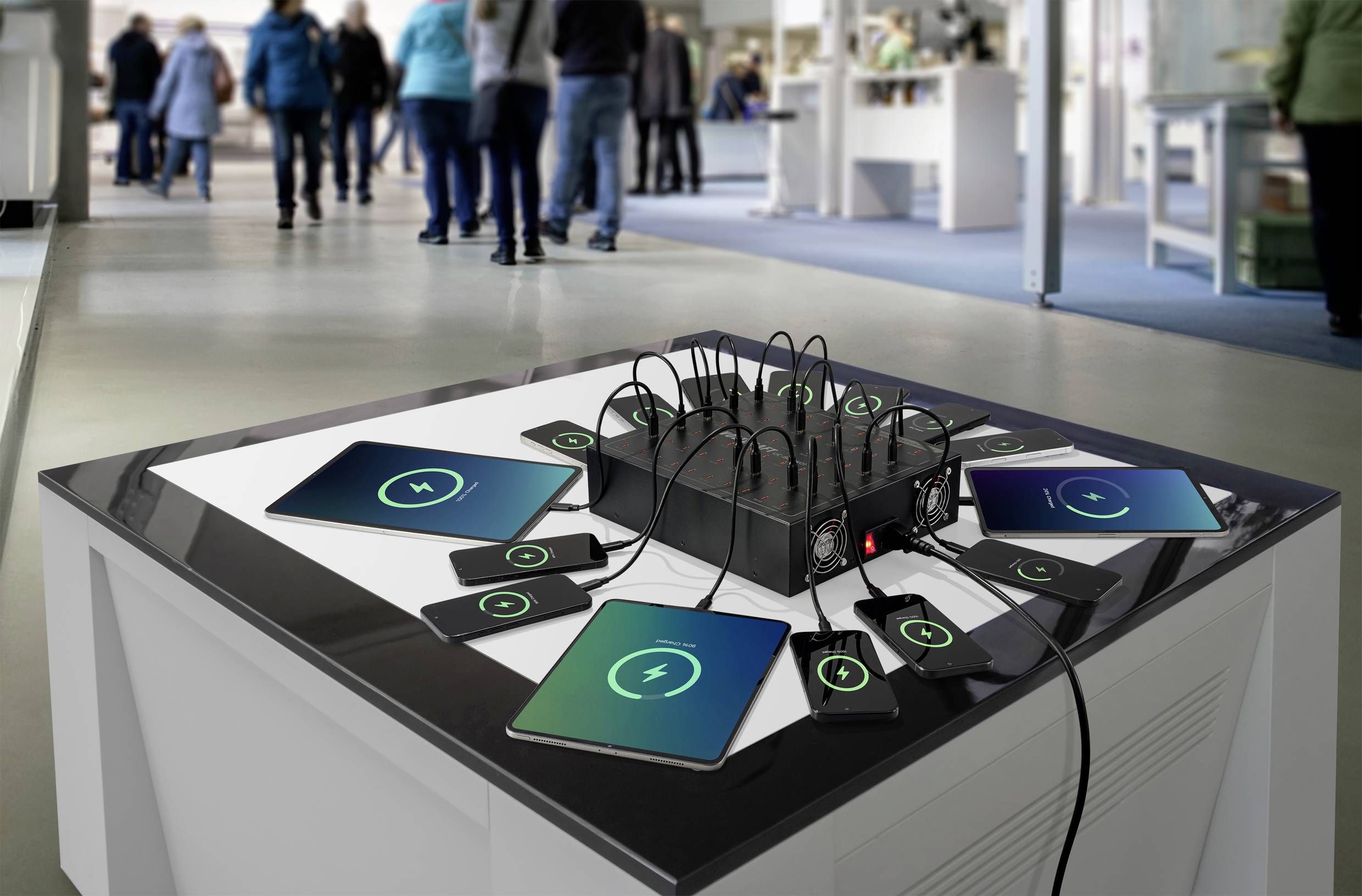 'Verschillende apparaten, waaronder tablets en smartphones, zijn verbonden met een centrale oplaadstandaard op een tafel in een technologiewinkromgeving.'