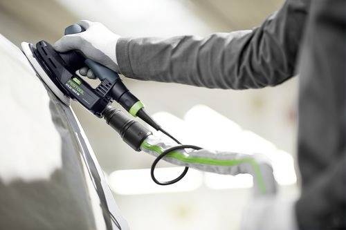 Een persoon gebruikt een draagbare elektrische polijstmachine op het oppervlak van een auto, wat wijst op automotive onderhoud of detailwerkzaamheden.