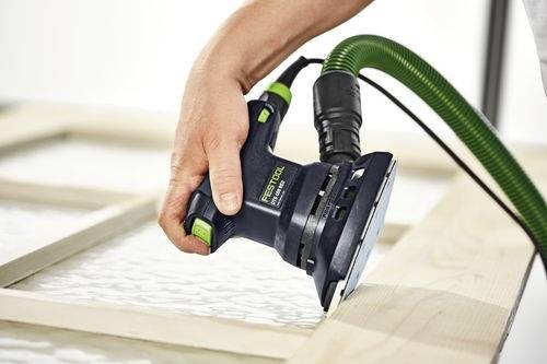 'Een persoon gebruikt een elektrische schuurmachine om een houten frame glad te schuren, met een groene stofzuiger-aansluiting die aan het gereedschap is bevestigd voor stofafzuiging.'