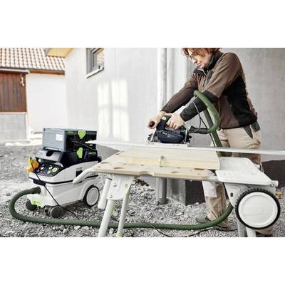 Een persoon die een elektrische zaag gebruikt om een houten plank door te zagen op een draagbare tafel. Een stofafzuiger is aangesloten en zichtbaar naast hen in de buitenlucht.