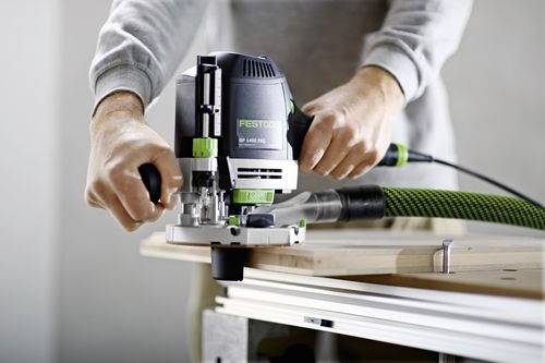 Een persoon bedient een draagbare elektrische bovenfrees op een houten plaat, met de nadruk op precisie en controle bij een houtbewerkingstaak.