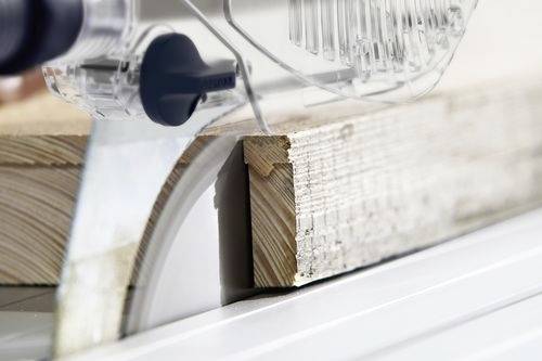 Een cirkelzaagblad dat door een stuk hout snijdt, waarbij houtbewerking of timmeren in een industriële omgeving wordt gedemonstreerd.