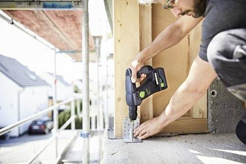 Een persoon gebruikt een boormachine om een metalen beugel aan een houten constructie te bevestigen, wat wijst op bouw- of renovatiewerkzaamheden in uitvoering.