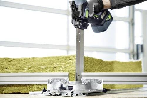 Een arbeider gebruikt een elektrisch gereedschap om een stuk isolatiemateriaal te snijden, waarbij metalen geleiders precisie waarborgen in een industriële omgeving.