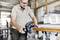 Een persoon met veiligheidsbril gebruikt een elektrisch gereedschap om een houten plank te schuren in een werkplaatsomgeving.
