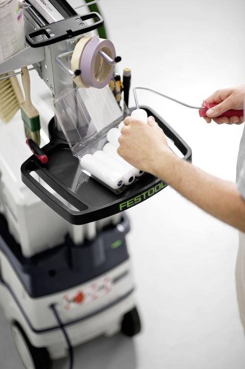 Een persoon rangschikt verfrollers op een werkkar die is uitgerust met verschillende gereedschappen en benodigdheden.