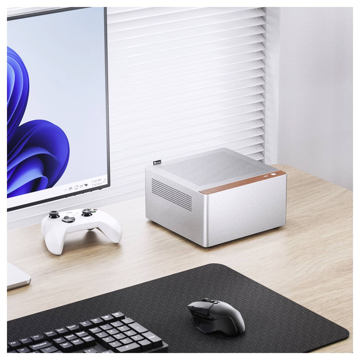 Een compacte, zilveren desktopcomputer op een houten bureau naast een monitor, gamecontroller en toetsenbord, in een moderne kantooromgeving.