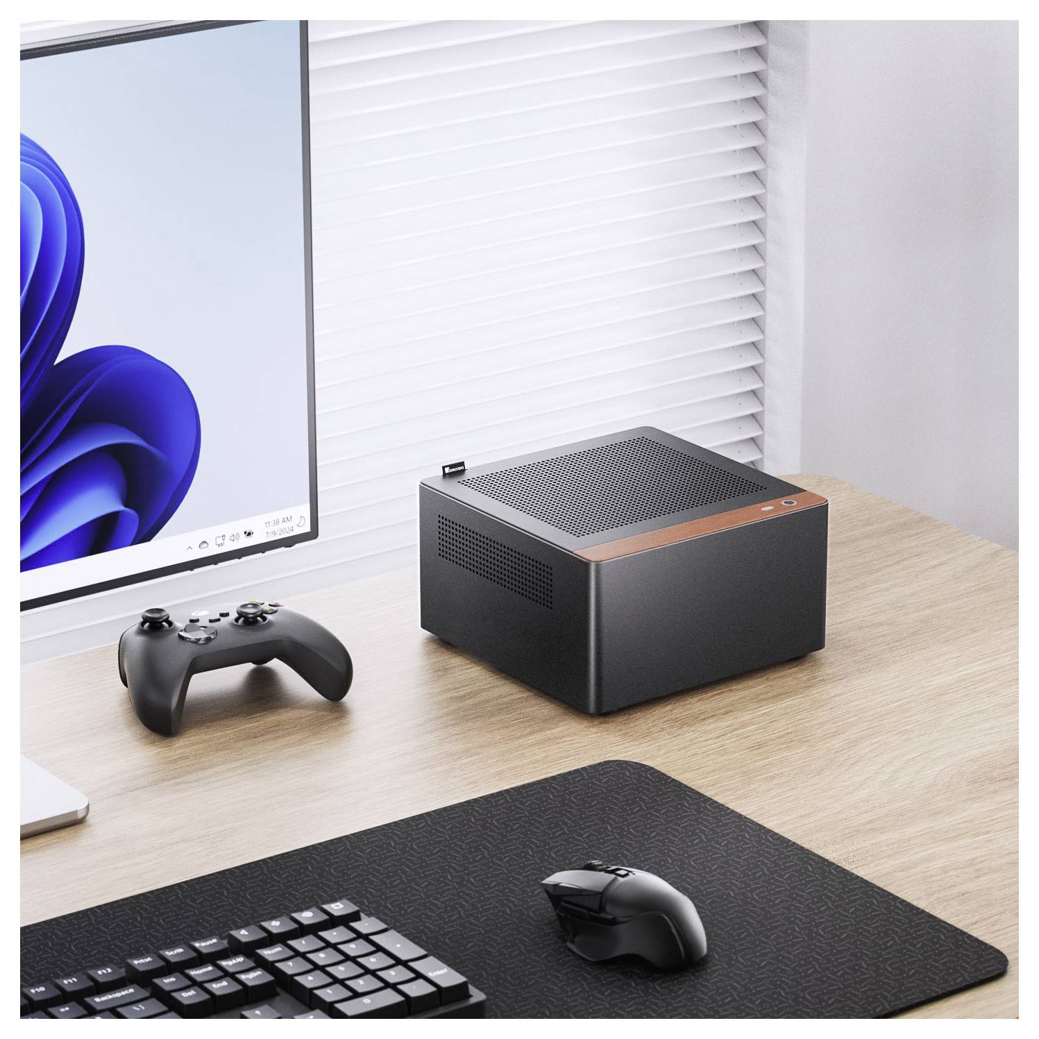 Een compacte zwarte en oranje mini-pc staat op een houten bureau naast een computermonitor waarop een blauw abstract logo en een gamecontroller worden weergegeven.