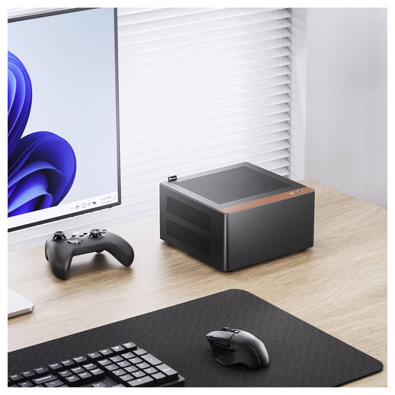 Een compacte, moderne desktopcomputer op een houten bureau naast een gamecontroller en toetsenbord. Een monitor toont een blauwe sluier-achtergrond.