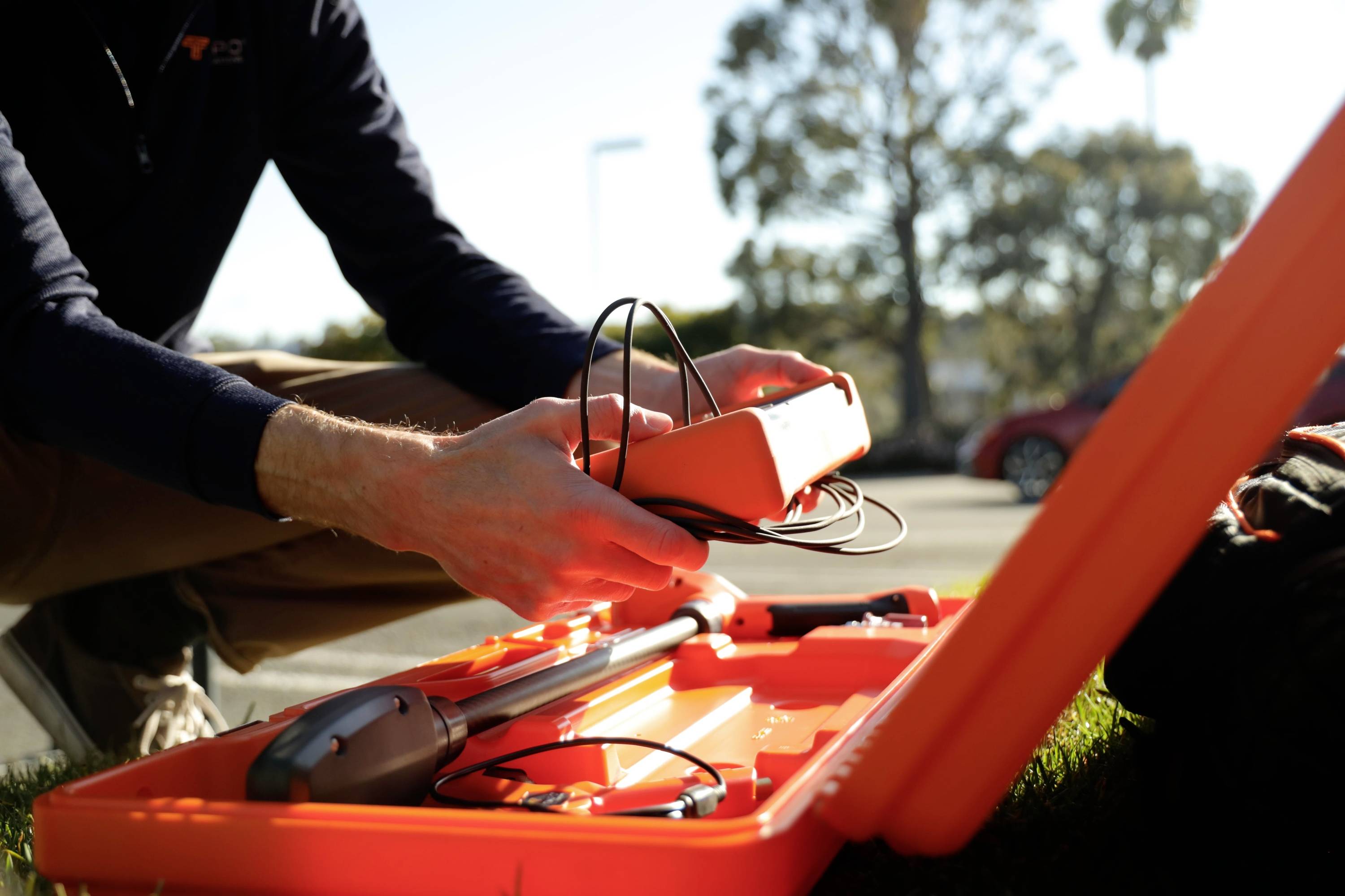 Een persoon stelt apparatuur bij in een open oranje behuizing buitenshuis, mogelijk bezig met de voorbereiding voor een technische installatie of veldwerk.