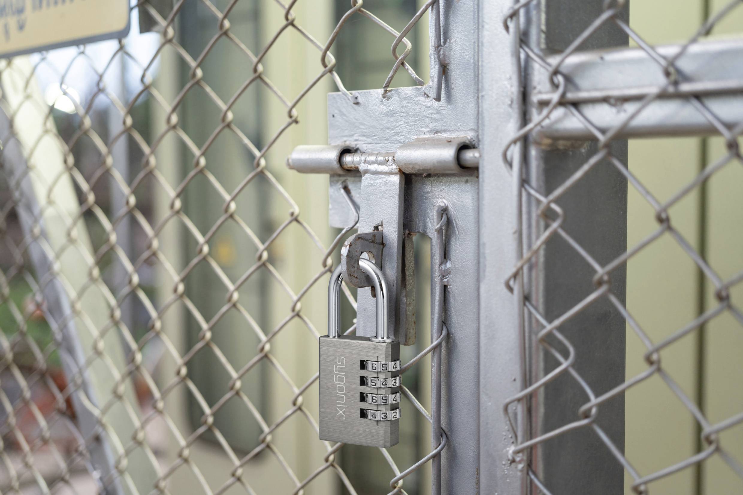 'Een zilverkleurig combinatieslot beveiligt een hek met mazen, wat beperkte toegang suggereert tot het omheinde gebied erachter.'