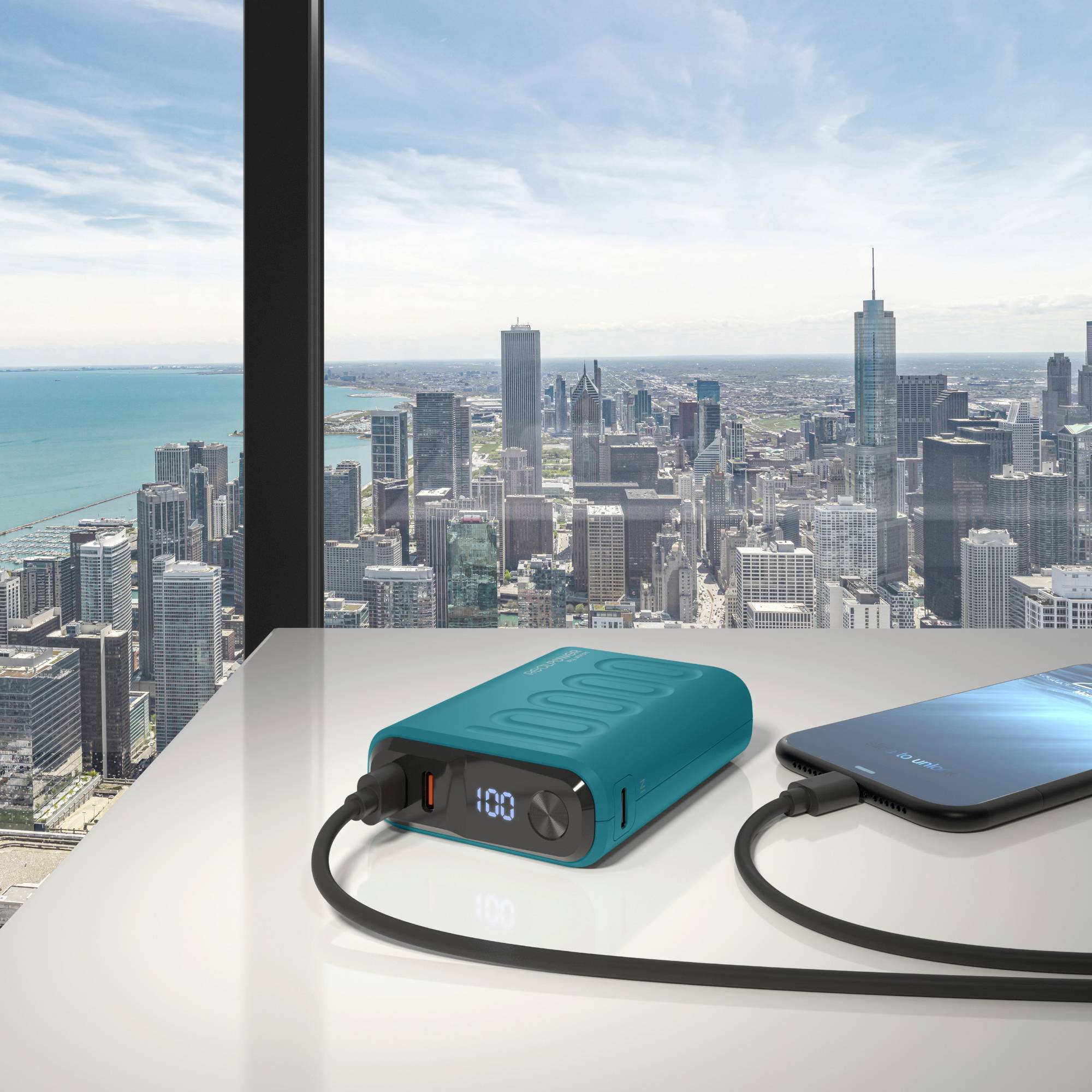Een powerbank laadt een smartphone op aan een tafel met een stadslandschap op de achtergrond door grote ramen.