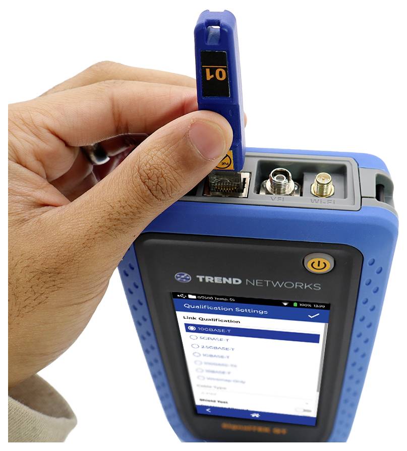 Een hand steekt een netwerkkabel in een blauw apparaat waarop 'Link Qualification' op het scherm wordt weergegeven, met verschillende aansluitpoorten zichtbaar.