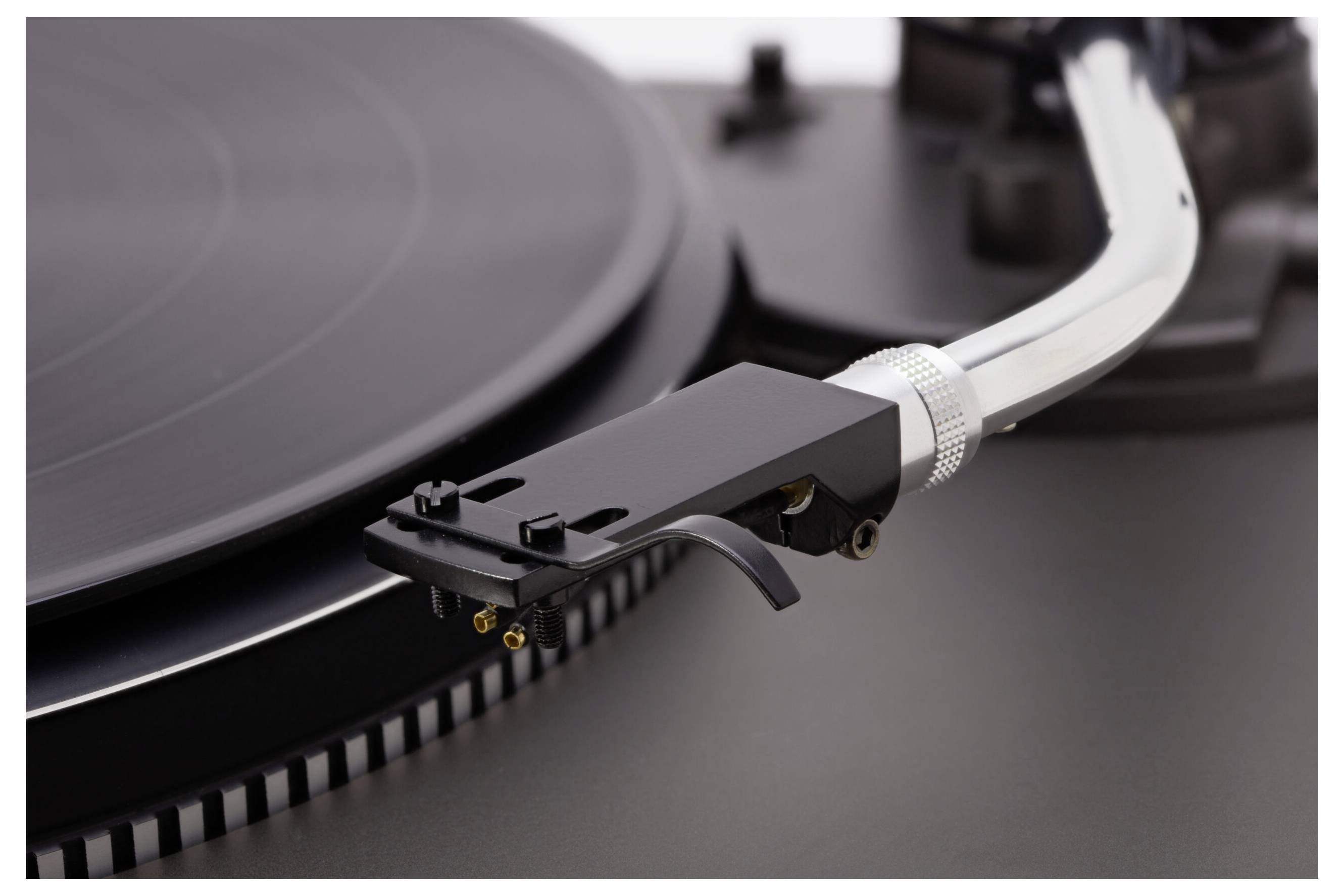 Close-up van een platenspeler met de focus op de naald en de pick-uparm boven een zwarte vinylplaat.
