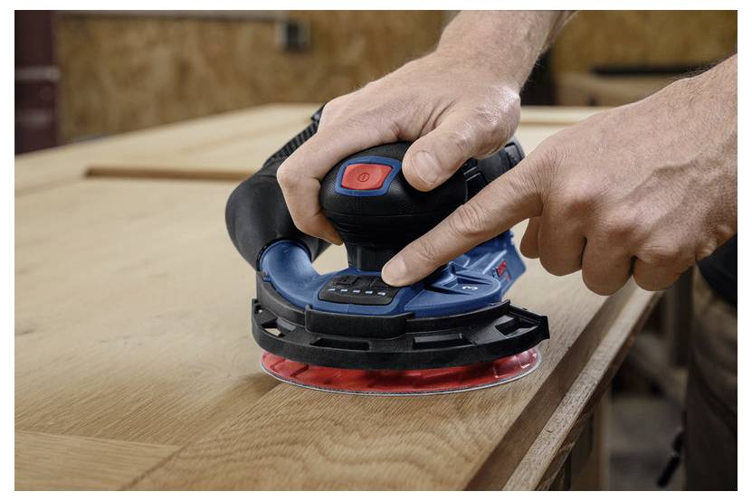 Een persoon gebruikt een draagbare elektrische schuurmachine op een houten oppervlak, waarbij druk wordt uitgeoefend om het hout glad te maken.