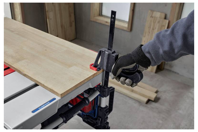 'Persoon die een klem gebruikt om een houten plank op een werkbank in een werkplaatsomgeving vast te zetten, draagt handschoenen voor veiligheid.'