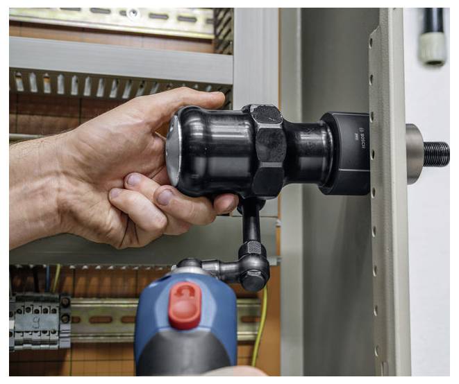 Een persoon die een gereedschap gebruikt met een rode knop om een grote zwarte buisaansluiting vast te zetten of af te stellen binnen een metalen frame, waarschijnlijk in een industriële omgeving.