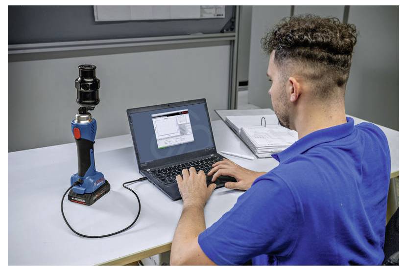 Een persoon in een blauw shirt gebruikt een laptop die is verbonden met een apparaat op een bureau, waarschijnlijk voor data-analyse of calibratiedoeleinden.
