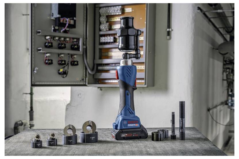 Een 'Bosch' gereedschap op een tafel met verschillende toebehoren. Een open elektrisch paneel is zichtbaar op de achtergrond, wat wijst op een reparatie- of installatieomgeving.