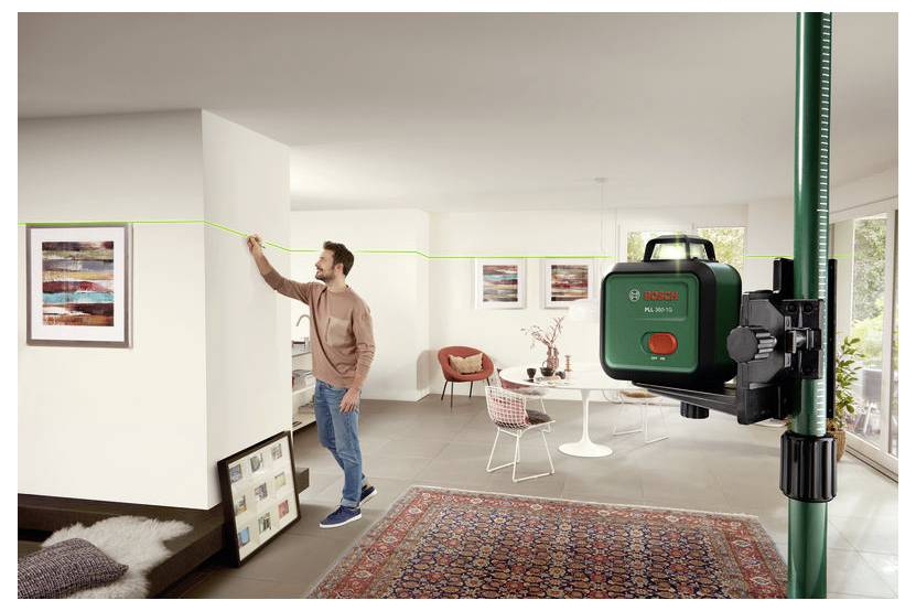 Een man gebruikt een Bosch lijnlaser om een rechte lijn op een muur te trekken in een moderne, stijlvol ingerichte woonkamer.