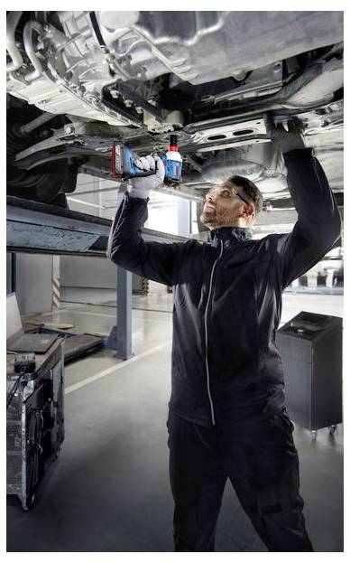 Een monteur in een werkplaats repareert de onderkant van een auto met behulp van een elektrisch gereedschap.