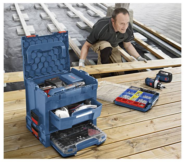 Een persoon die een houten terras assembleert nabij water, met een openstaande gereedschapskist waarop verschillende gereedschappen zijn uitgestald en een boormachine naast een doos met schroeven.