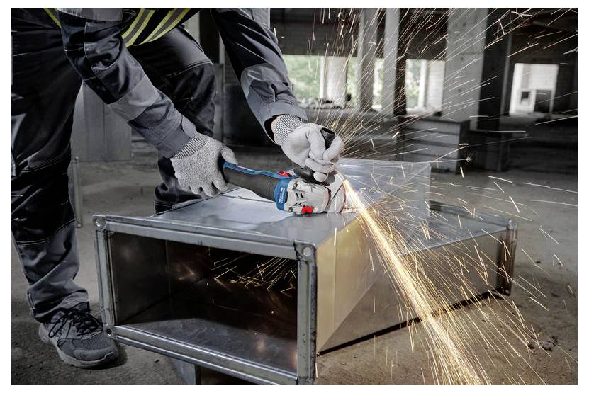 Een persoon met beschermende handschoenen bedient een haakse slijper, waarbij vonken vrijkomen, terwijl hij een metalen kanaal in een industriële omgeving doorsnijdt.