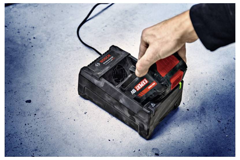 Een hand die een Bosch-accu in een oplader plaatst op een betonnen oppervlak.