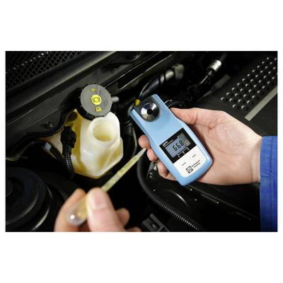 Een persoon die een digitale refractometer vasthoudt met een aflezing van 6,8 naast een open koelvloeistof reservoir in de motorruimte van een auto.