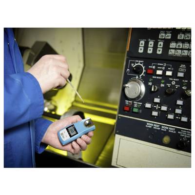 'Een persoon in een blauwe jas houdt een digitale refractometer in de buurt van machinerie, waarbij de vloeistofconcentratie wordt gemeten. Het scherm van het apparaat toont aflezingen.'