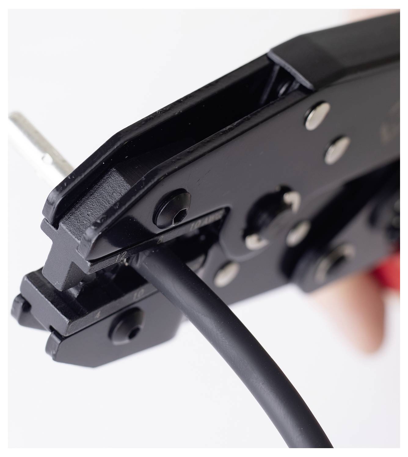 Een close-up van een zwarte krimptang die een zwarte kabel vasthoudt, gebruikt voor het aansluiten van elektrische draden, vastgehouden door een persoon op de achtergrond.
