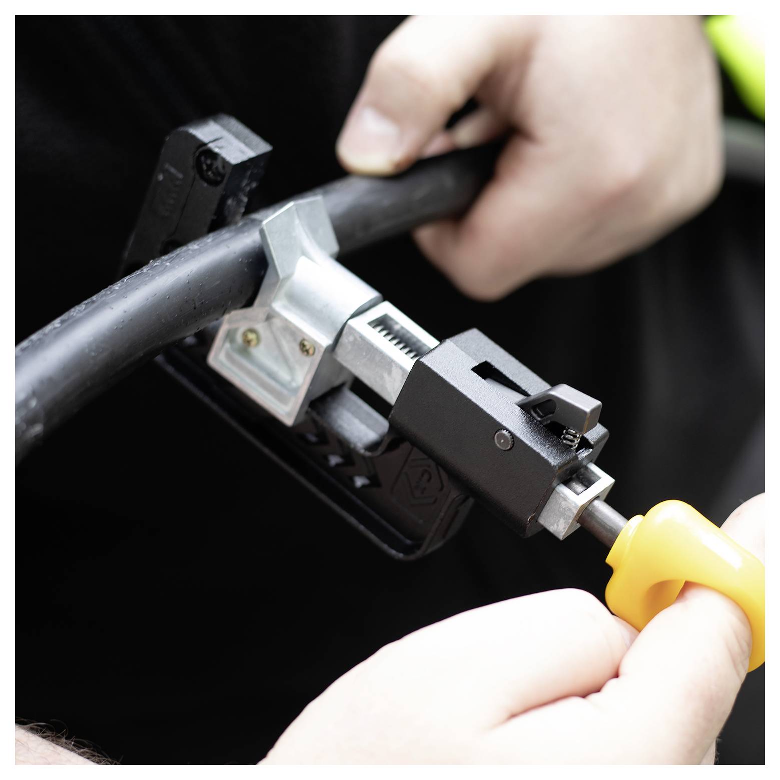 Twee handen gebruiken een gereedschap om de isolatie van een dikke zwarte kabel te verwijderen, ter voorbereiding op verdere werkzaamheden.