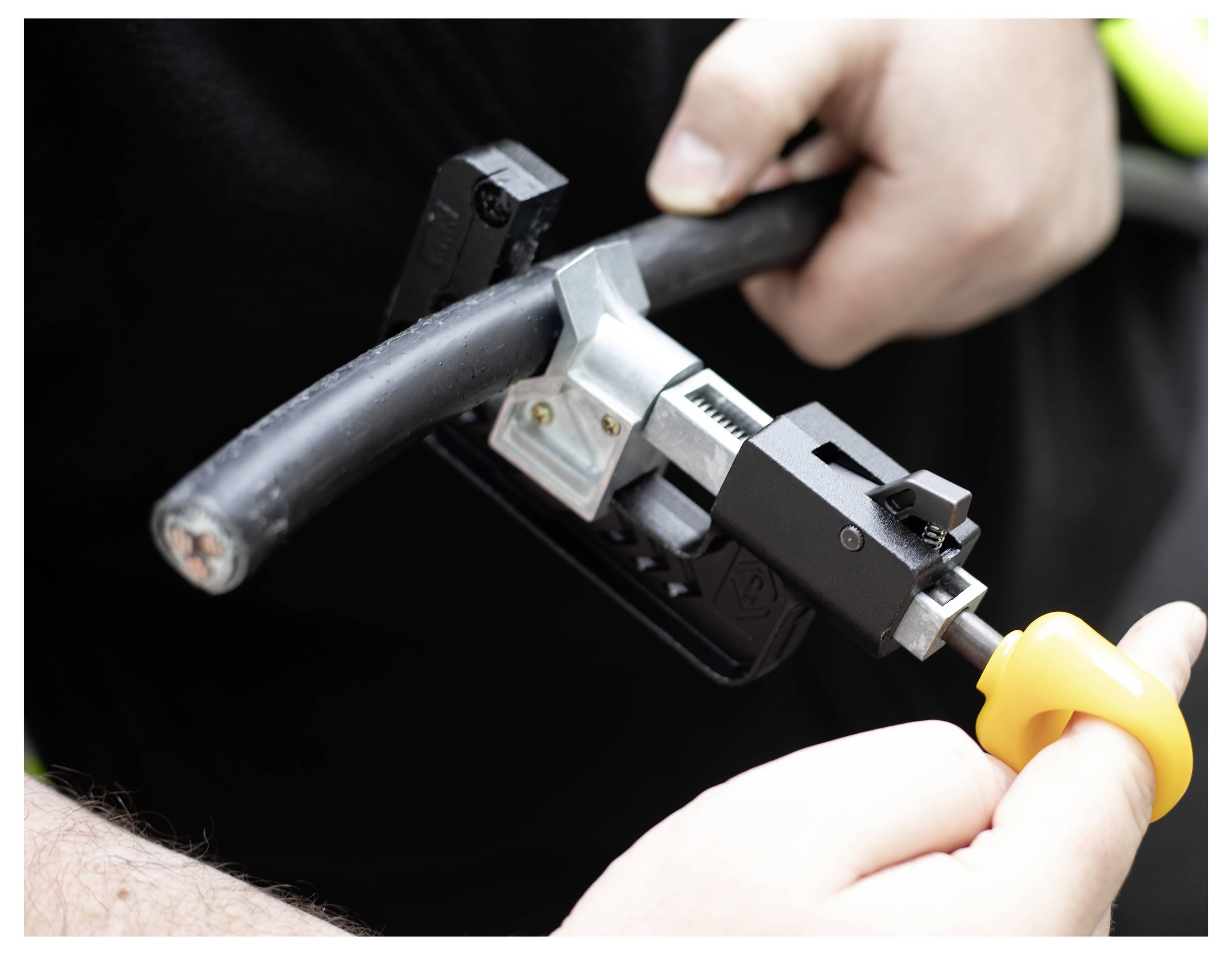 Handen die een gereedschap gebruiken om een dikke zwarte kabel te strippen, waarbij de focus ligt op het proces van het blootleggen van de interne draden voor elektrotechnisch werk.