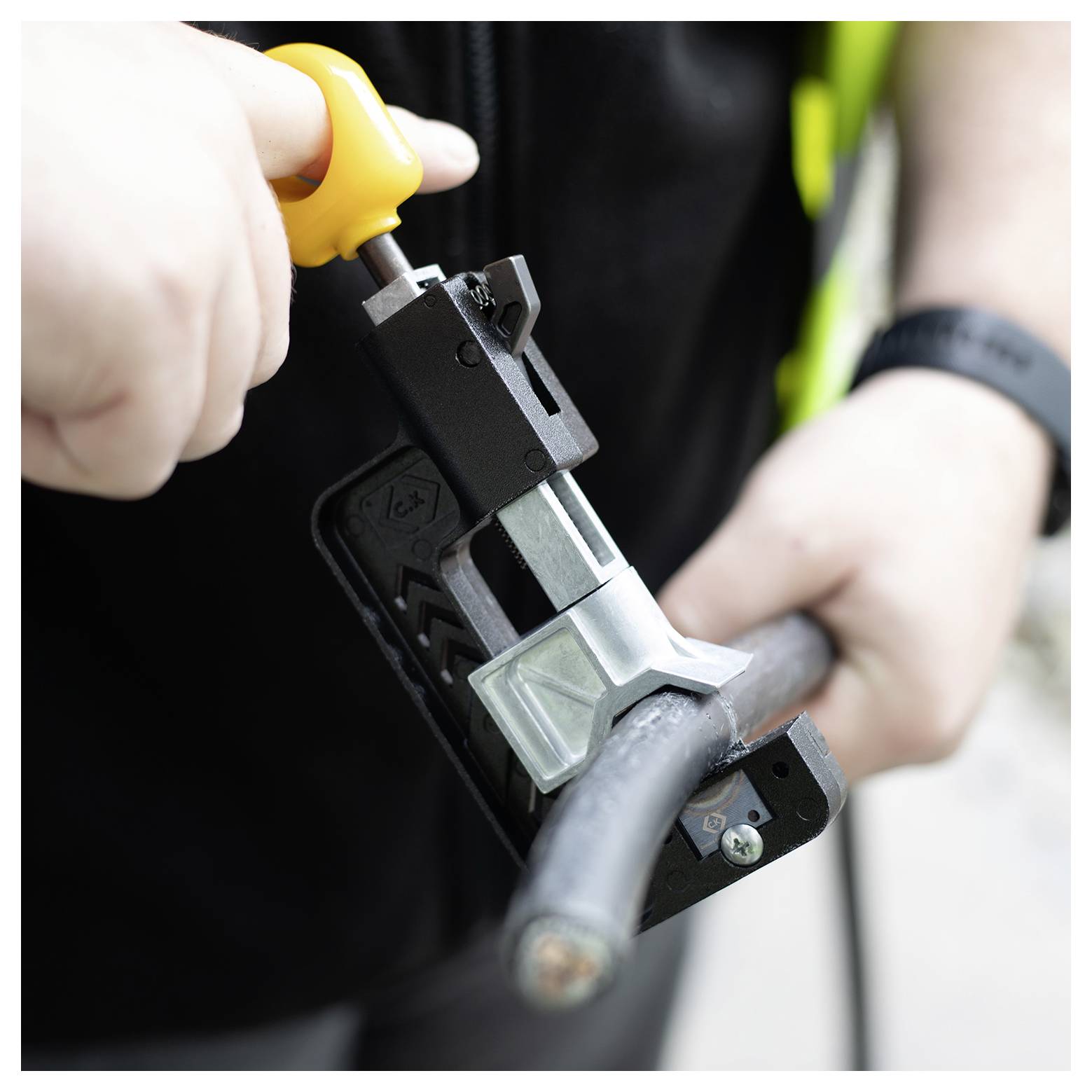 Een persoon knipt een zwarte kabel door met een kabeltang met gele handvatten, waarbij het gebruik van een gespecialiseerd gereedschap voor kabelbehandeling wordt gedemonstreerd.