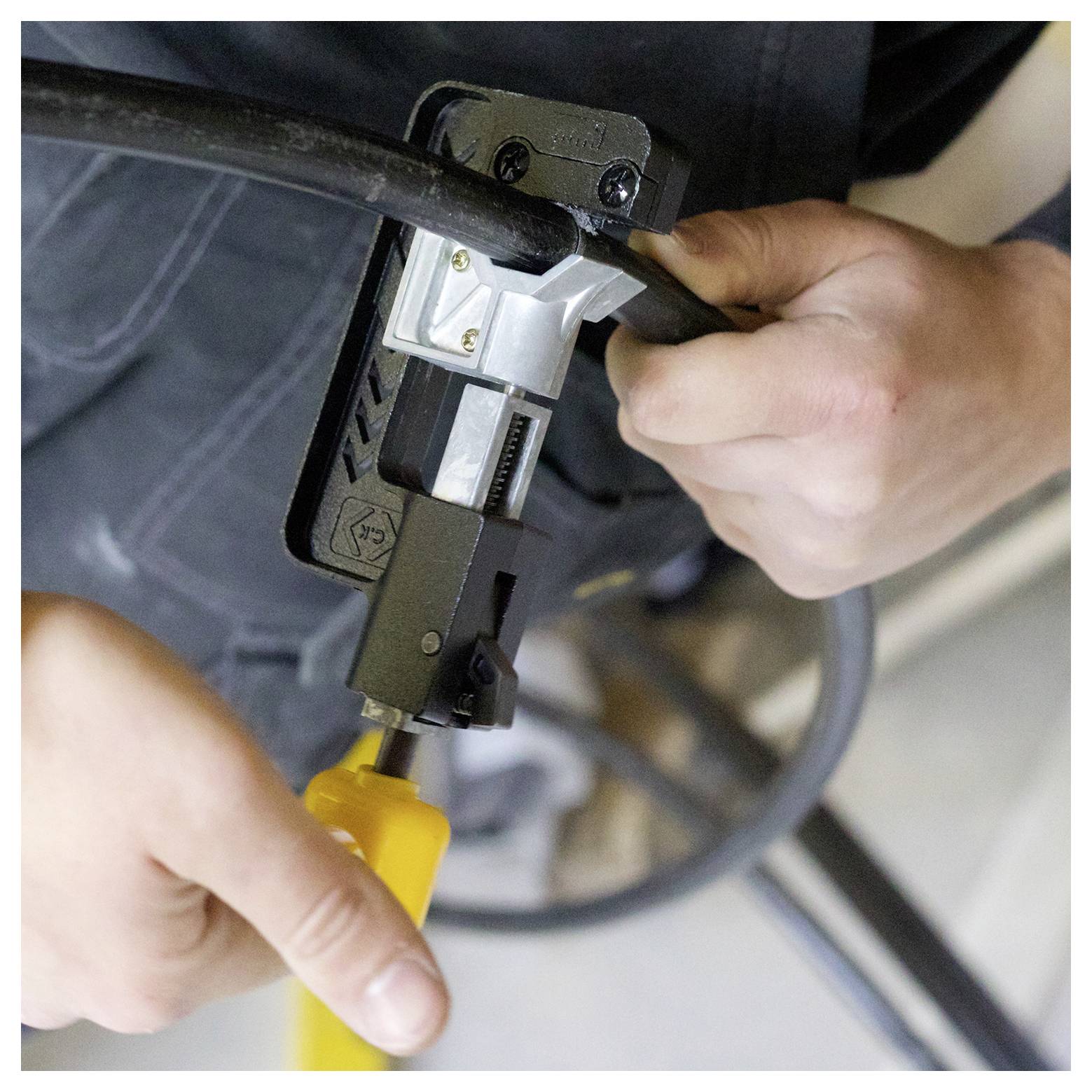 Persoon spant een kabelconnector aan met een gereedschap, met de focus op het verzekeren van een vaste verbinding. De taak vereist twee handen en een zwarte kabel.