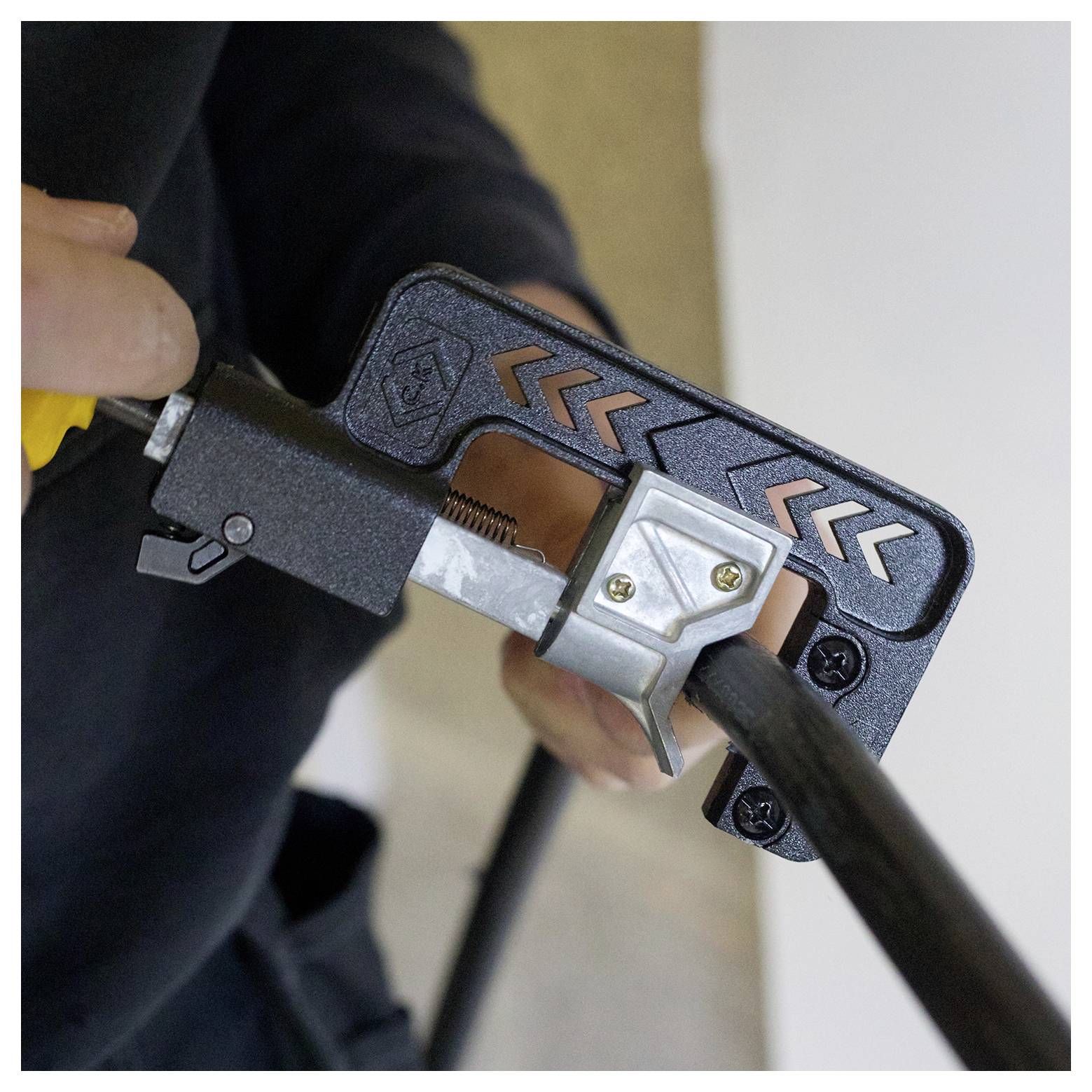 Een persoon die een kabelstripper gebruikt om de buitenste laag van een zwarte kabel te verwijderen, wat een stap aangeeft bij kabelinstallatie of -reparatie.