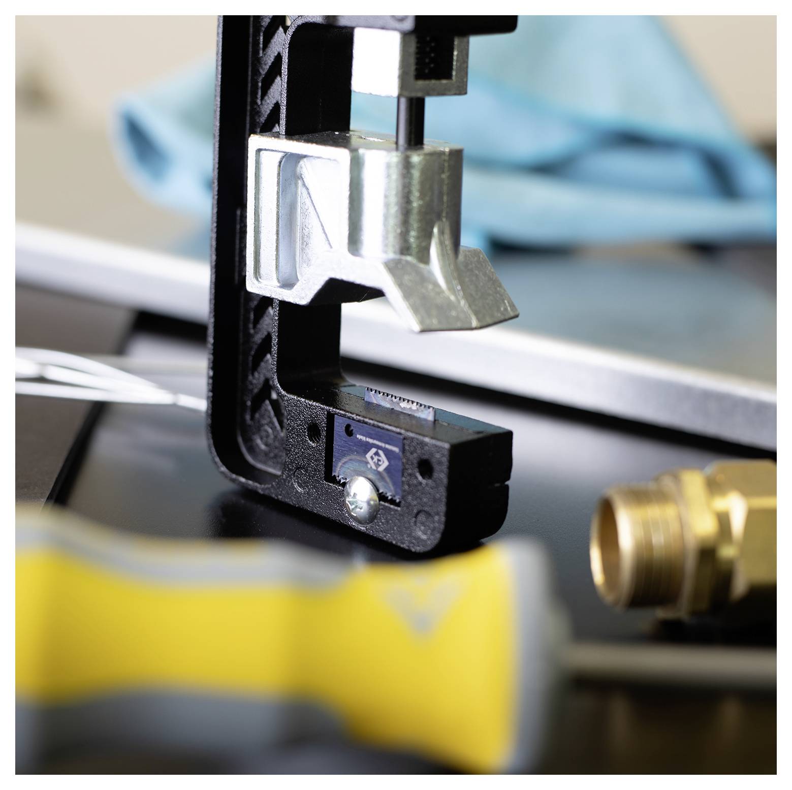 Een close-up van een C-klem die metalen onderdelen op een werkbank vasthoudt, met gereedschappen en bouten in de nabijheid, wat wijst op een mechanische montagetaak.