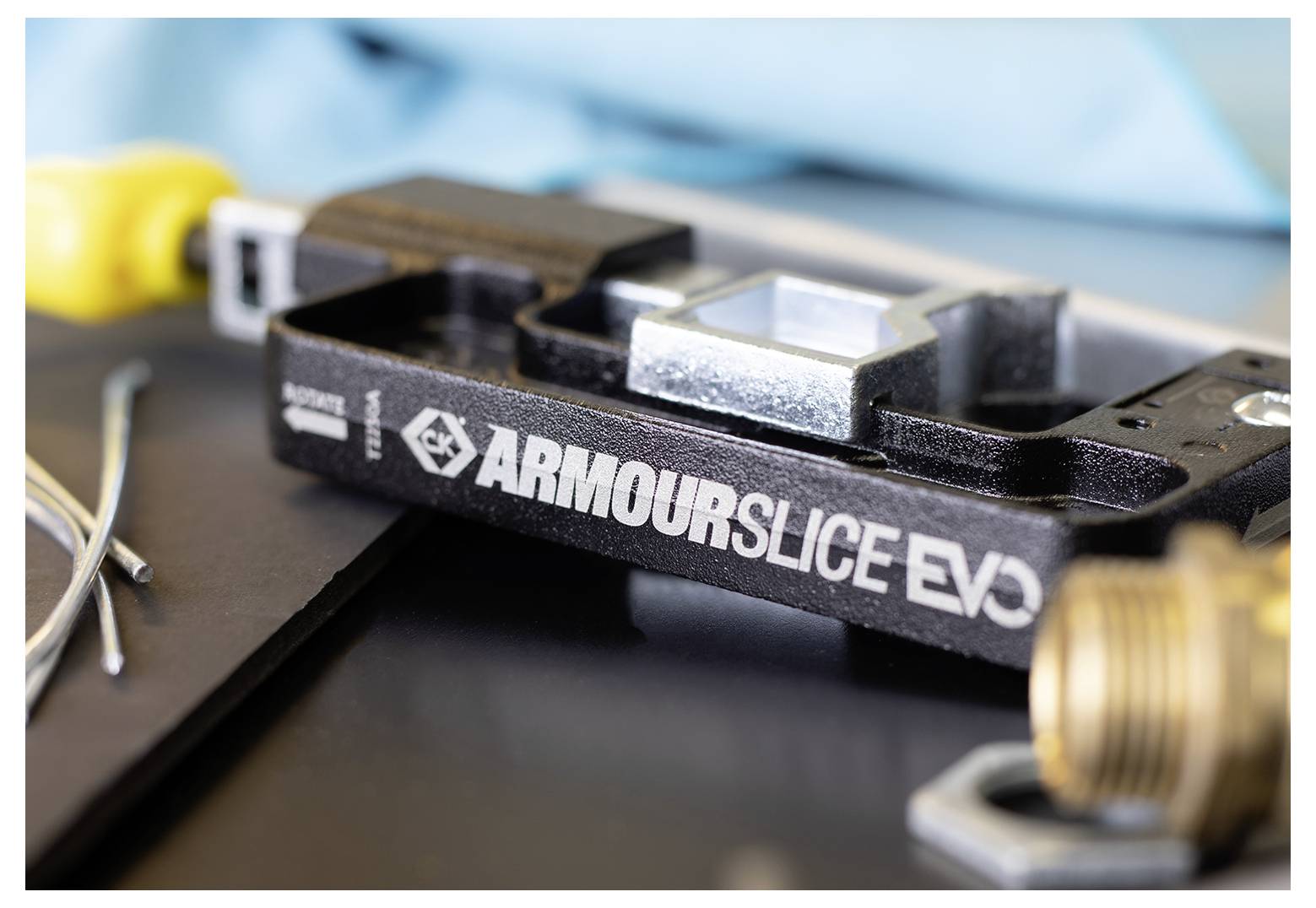 Close-up van een zwart gereedschap gelabeld 'ArmourSlice EVO' met een metalen bevestiging en draden in de nabijheid, wat wijst op gebruik in elektrotechnisch werk.