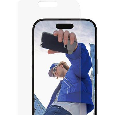 Een persoon met een blauwe jas en zonnebril maakt een selfie met een smartphone, staande voor moderne glazen gebouwen onder een heldere lucht.