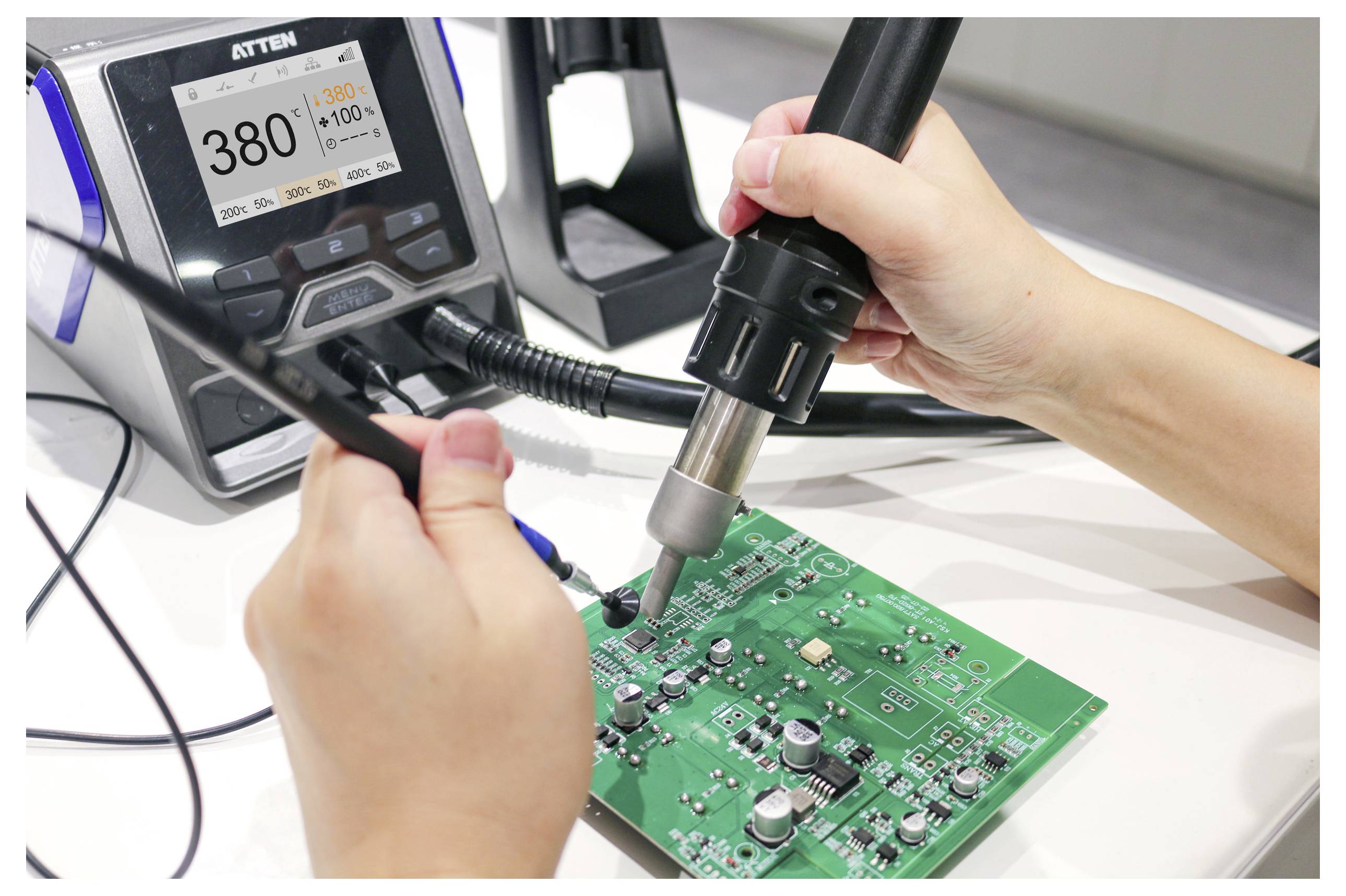 Een persoon gebruikt een heteluchtpistool en pincetten om te werken aan een groen printplaatje. Een digitaal temperatuurdisplay toont '380°C' naast de werkplek.