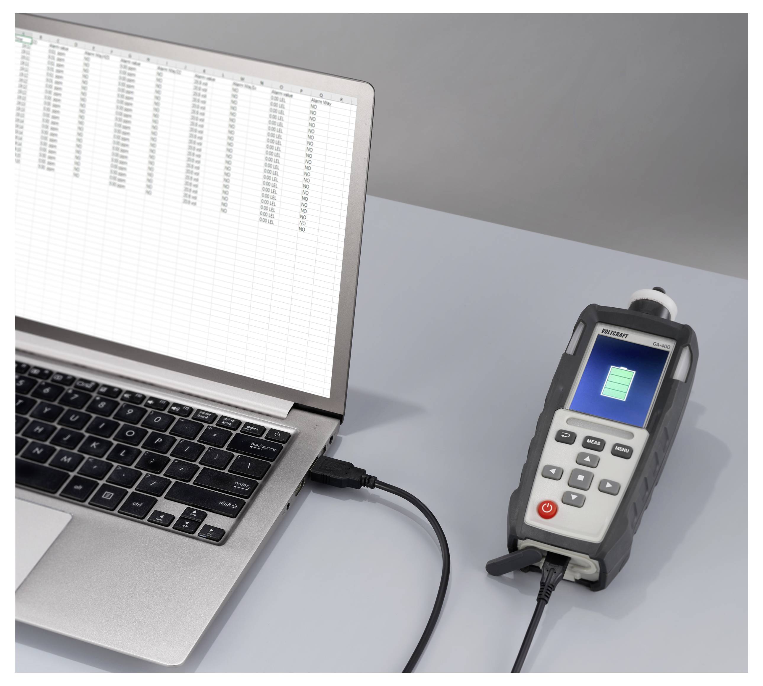 'Een laptop met een geopend spreadsheet is via een kabel verbonden met een handheld apparaat dat een groen batteriijpictogram op het scherm weergeeft.'