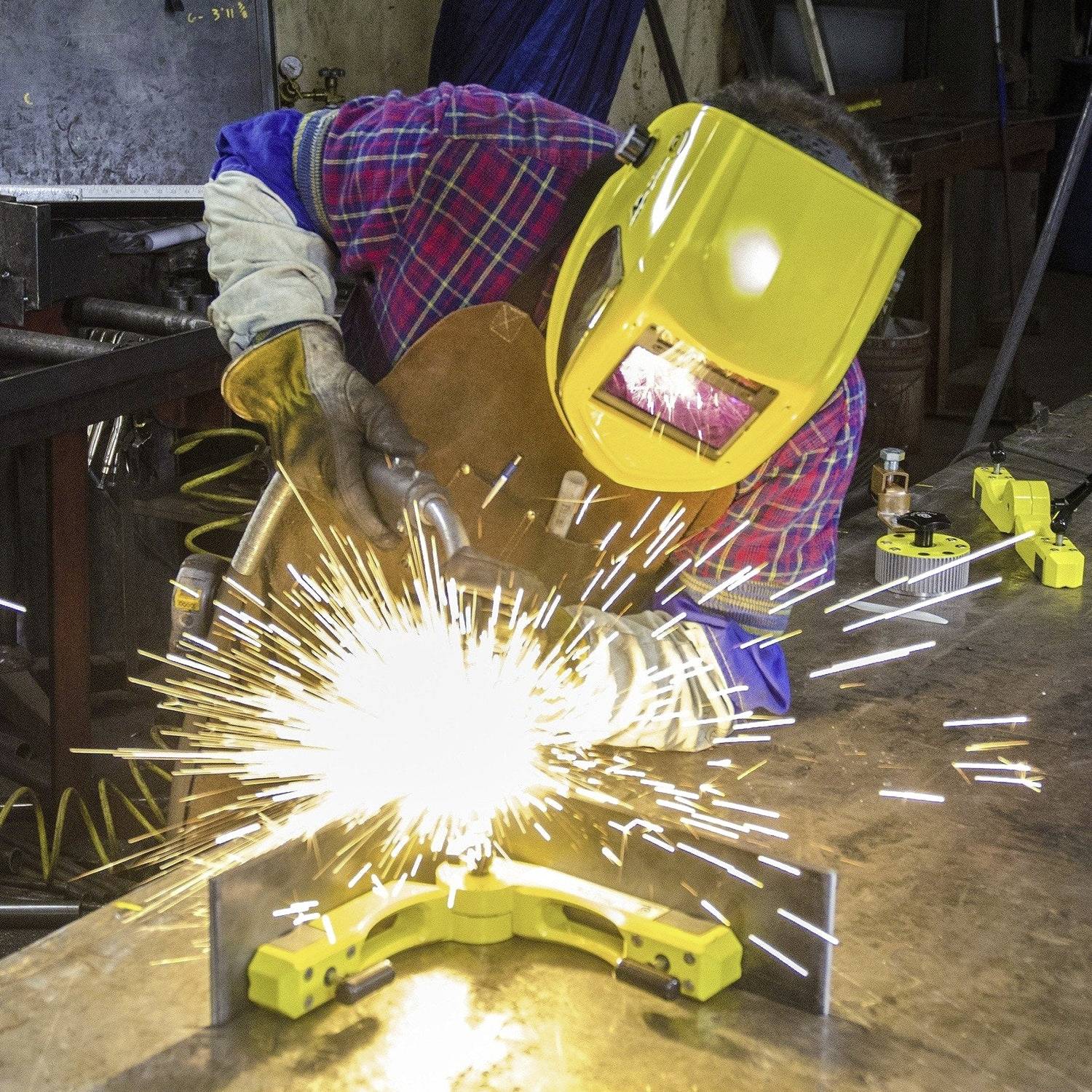 Een persoon is metalen onderdelen aan het lassen in een werkplaats, draagt een beschermende helm en handschoenen. Felle vonken zijn zichtbaar.