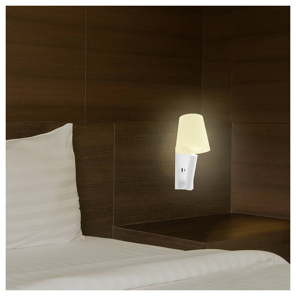 Een vaag verlichte beige lamp is bevestigd aan een donkeren houten muur boven een wit kussen en linnengoed op een bed, waardoor een rustige en gezellige sfeer ontstaat.